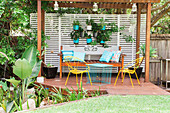 Pergola with wooden bench, metal chairs, table and hanging plant pots