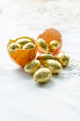 Gefärbte Eierschalen eines leeren Ostereis gefüllt mit Schokoladeneiern in Goldfolie