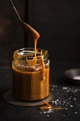 A jar of salted carmel sauce with a spoon, dark background