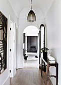 White hallway with antique console table and pendant lamp, open arched door to living room