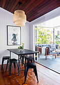 Black metal stools around the dining table in front of the terrace with a sofa