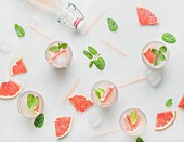 Flat-lay of cold refreshing summer alcohol cocktail with fresh grapefruit, mint and ice over white marble background