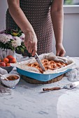 Frau schneidet Aprikosen-Joghurt-Kuchen in Stücke