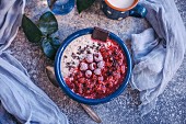 Porridge with raspberry sauce topped with frozen raspberries, cacao nibs and dark chocolate in a blue bowl