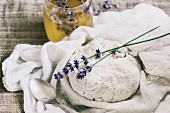 Selbstgemachter Hüttenkäse im Leinentuch, dahinter Honig mit Lavendelblüten