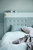 Button-tufted bed headboard against partition wall below sloping ceiling
