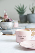 Rosafarbene Tasse mit Schrift auf gedecktem Tisch