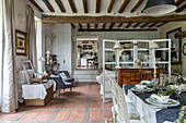 Dining area with terracotta floor riles, wood-beamed ceiling, chest of drawers and partition screen in rustic interior