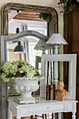 Flowers in urn, bust, picture frame and table lamp on console table in front of mirrors