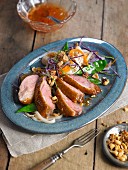 Sliced duck breast on rice noodles with a vegetable garnish