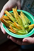 A woman holding a green antique dish with zucchini blossoms