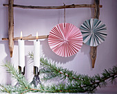 Paper rosettes hung from wooden ladder next to candles on conifer branch