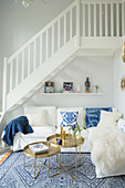 White couch with scatter cushions and set of round tray tables below staircase