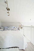 Doppelbett mit weißer Tagesdecke und weiß-blauen Kissen auf Galerie
