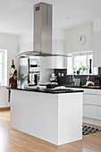 weiße Küche mit schwarzem Fliesenspiegel, Abzugshaube über Kücheninsel