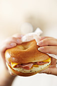 Hands holding an egg, ham and cheese bagel
