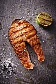 A grilled salmon steak with half a lime, salt and pepper