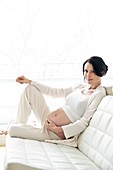 Pregnant woman on sofa touching tummy