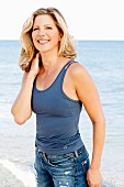A blonde woman on a beach wearing a blue vest top and jeans