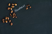 Hazelnuts, whole and hulled, arranged around the German word for hazelnut written in chalk on a blackboard