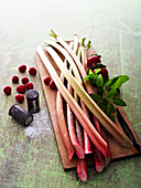 Rhubarb spears on a wooden board with raspberries next to it