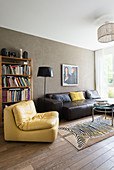 Yellow leather easy chair and black leather couch in front of bookcase in living room with olive-green wall