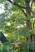 Floating candles, hollyhock and hydrangea flowers in DIY birdbath hung from tree on long ropes