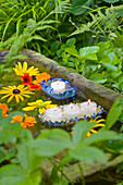 DIY Schwimmlichter aus Fischdosen mit Fransen und Blüten in einem Sandsteintrog