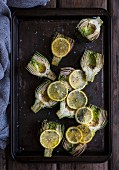 Artichokes with lemon slices on a baking tray