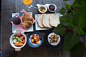 A breakfast with fruit salad, yoghurt and muesli, a croissant, white bread and jam