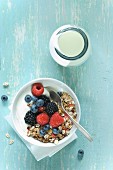 Yoghurt and muesli with berries in a bowl next to a glass bottle of yoghurt