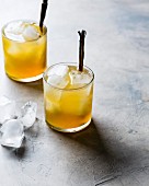 Two Golden Whiskey cocktails with cinnamon stick and ice cubes