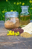 Mustard seeds, mustard flour, mustard oil and mustard flowers on a wooden table