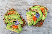 Wholegrain bread topped with avocado slices, tomato and borage flowers