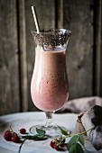 A vegan raspberry smoothie in a glass with chia seeds around the rim
