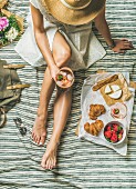 Frau im Kleid mit Weinglas, Erdbeeren und Croissants auf Picknickdecke