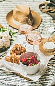Rosé wine, strawberries, croissants, flowers and a straw hat on a picnic blanket