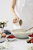 How to make bread pudding with berries: a woman pouring maple syrup into the egg and milk mix