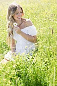 Woman sitting in meadow holding daisy