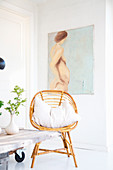 Rattan chair with cushions in front of nude artwork