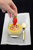 A hand placing a strawberry on a crème brulée