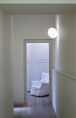 Blick durch den Flur und offene Tür auf einen weißen Sessel