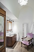Old armchair with pink upholstery and dark wooden furnishings in bathroom