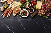 Italian snacks food with Ham, Sliced bread Ciabatta, Olives, Parmesan cheese, Grissini bread sticks, Feta cheese with dried tomatoes and Sausage on dark marble background