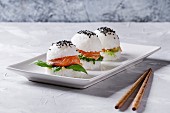 Mini rice sushi burgers with smoked salmon, green salad and sauces, black sesame served on white square plate