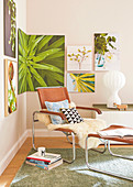 A sheepskin rug and cushions on a leather armchair with a matching footstool in the corner of a room with pictures of plants on the wall