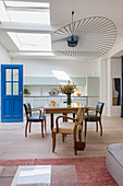 Armchairs around dining table below designer lamp in front of mint-green kitchen counter