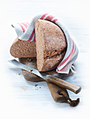Wholemeal wheat bread on a chopping board with a knife and a tea towel
