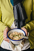 A woman holding a bowl of risotto with thyme and parmesan
