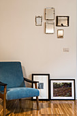 Blue armchair next to framed photos and collection of mirrors mounted on wall